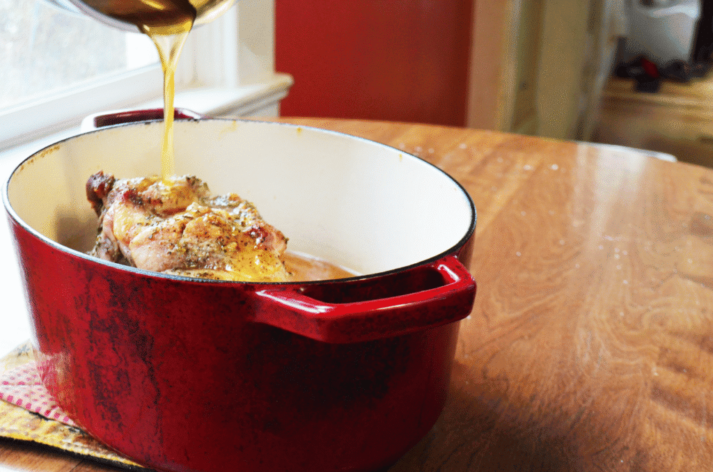 a honey maple glaze is poured over raw pork shoulder in a dutch oven.