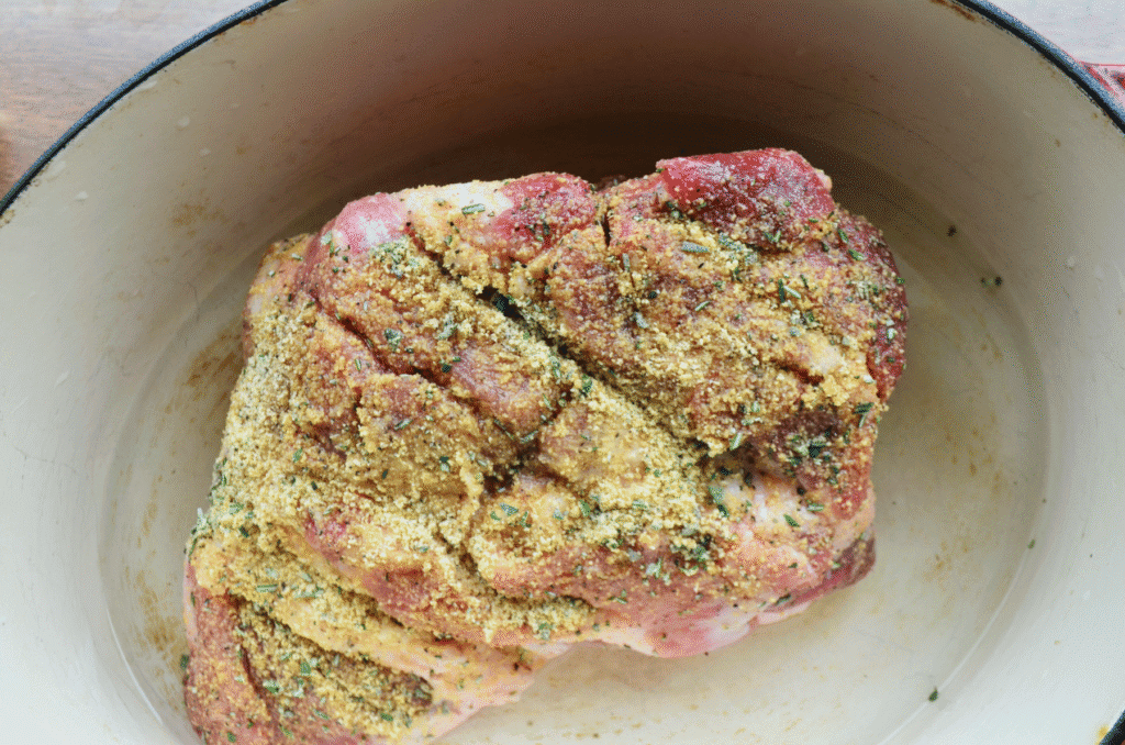 a raw pork shoulder with a scored crisscross pattern is covered in herbs.