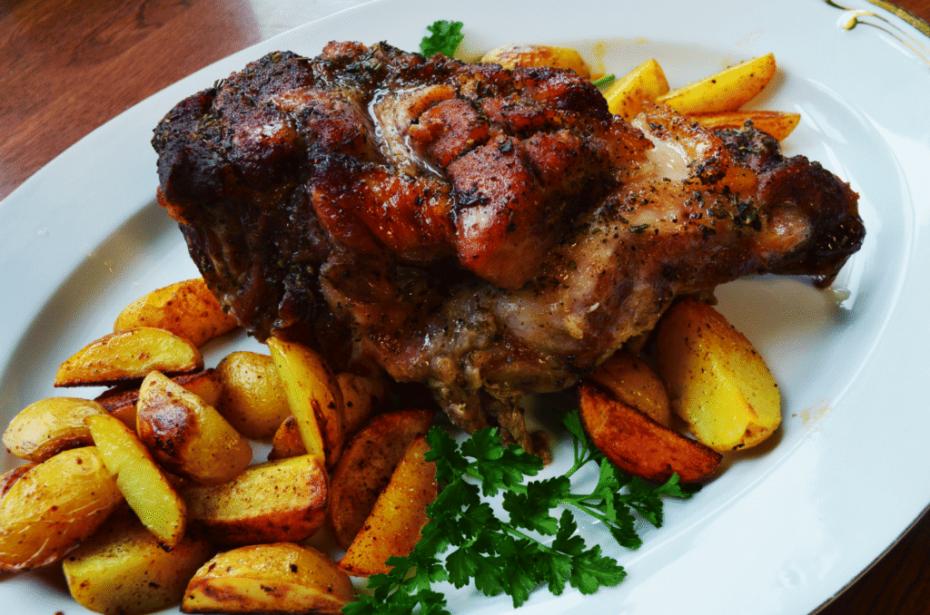 a warm honey glazed pork shoulder sits on a serving platter next to roasted potatoes.