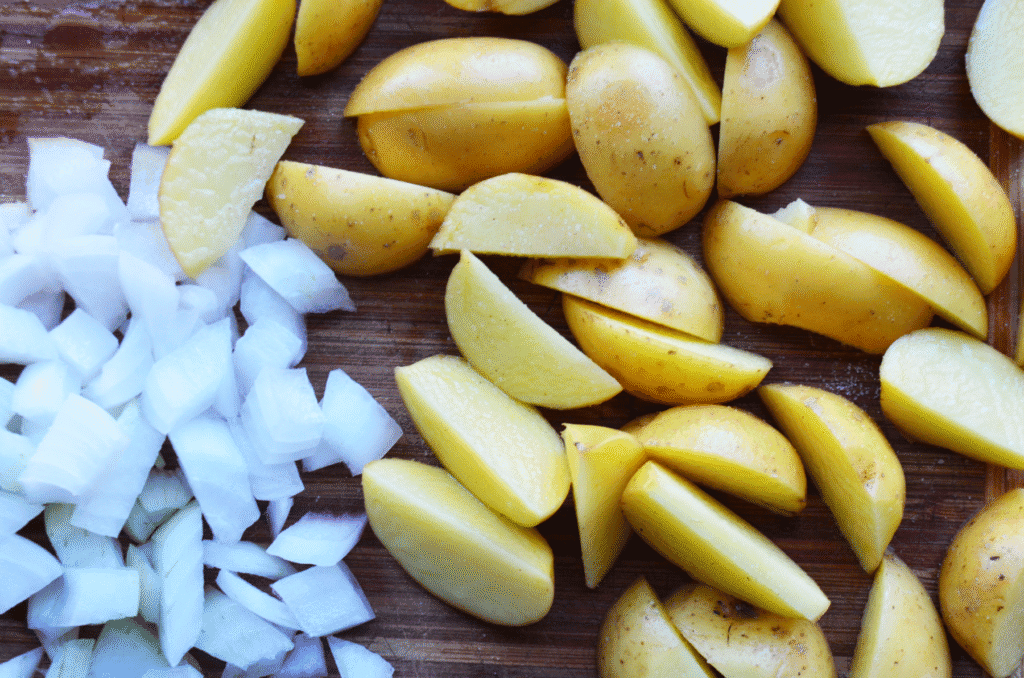 Raw potato wedges and diced onion on a cutting board for cast iron skillet fired potatoes in the oven