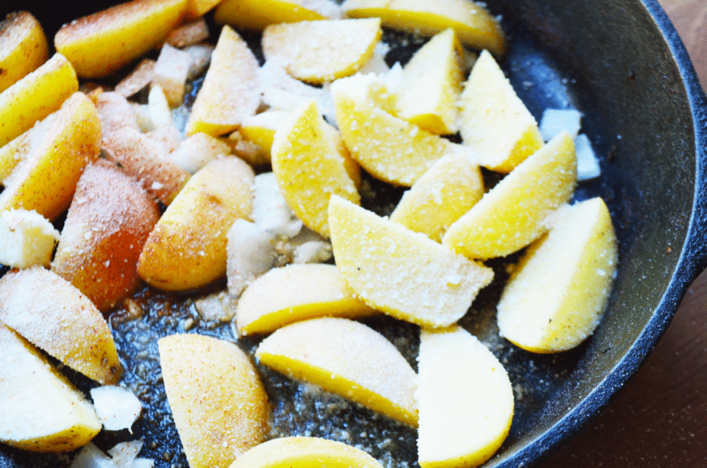 Raw pieces of potato ready to cook in the iron skillet with seasoning and bread crumbs