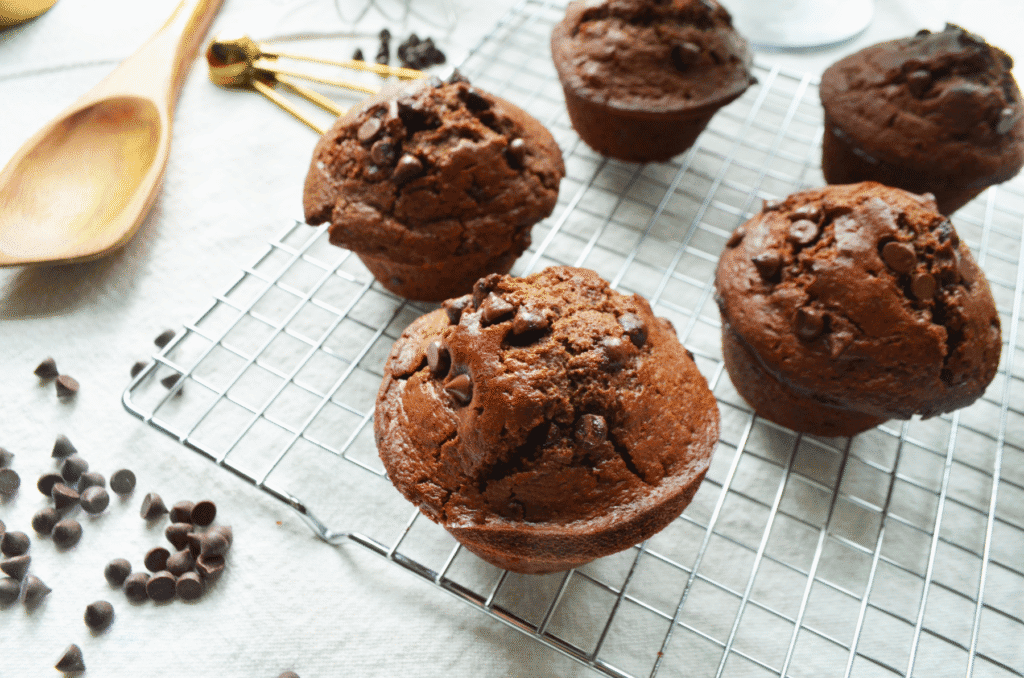 Double chocolate sourdough einkorn muffins cool on a wire rack next to spilled mini chocolate chips.
