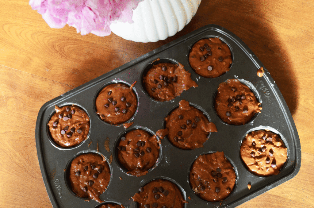 Muffin pan on counter top with chocolate muffins batter unbaked inside the pan
