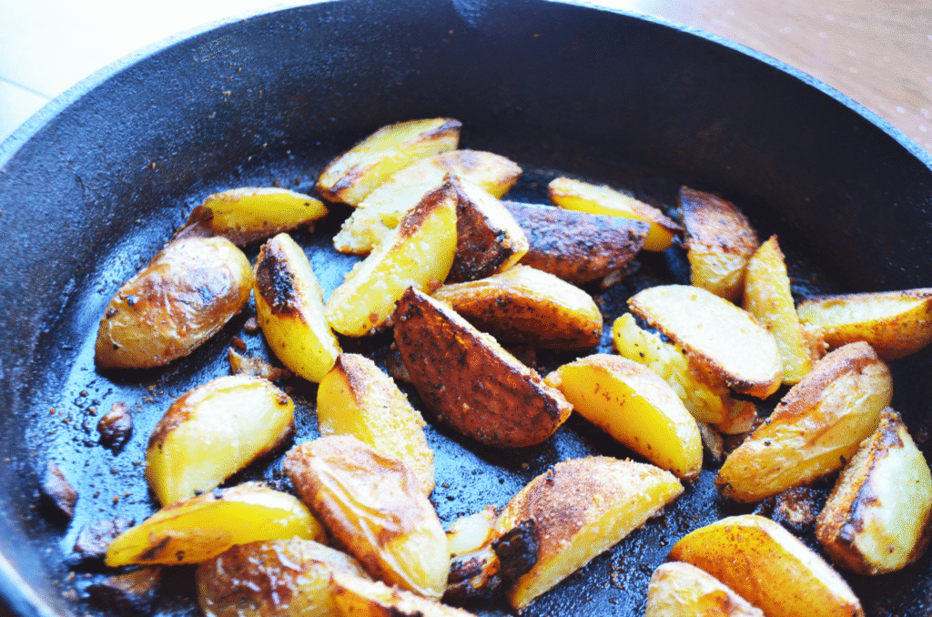 A cast iron skillet with cooked potato wedges that are nicely browned