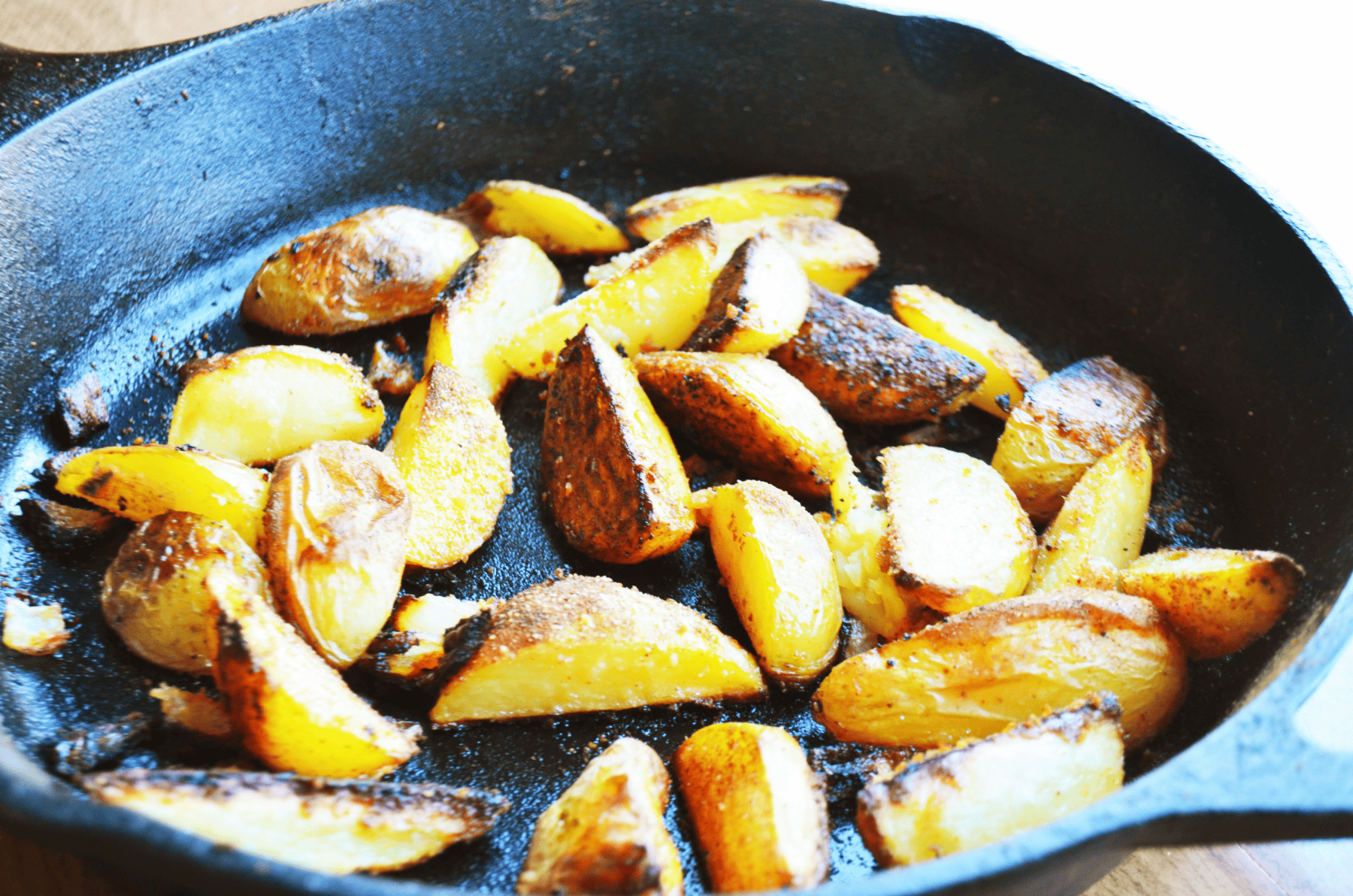 Browned fried potato slices sizzle in a cast iron pan.